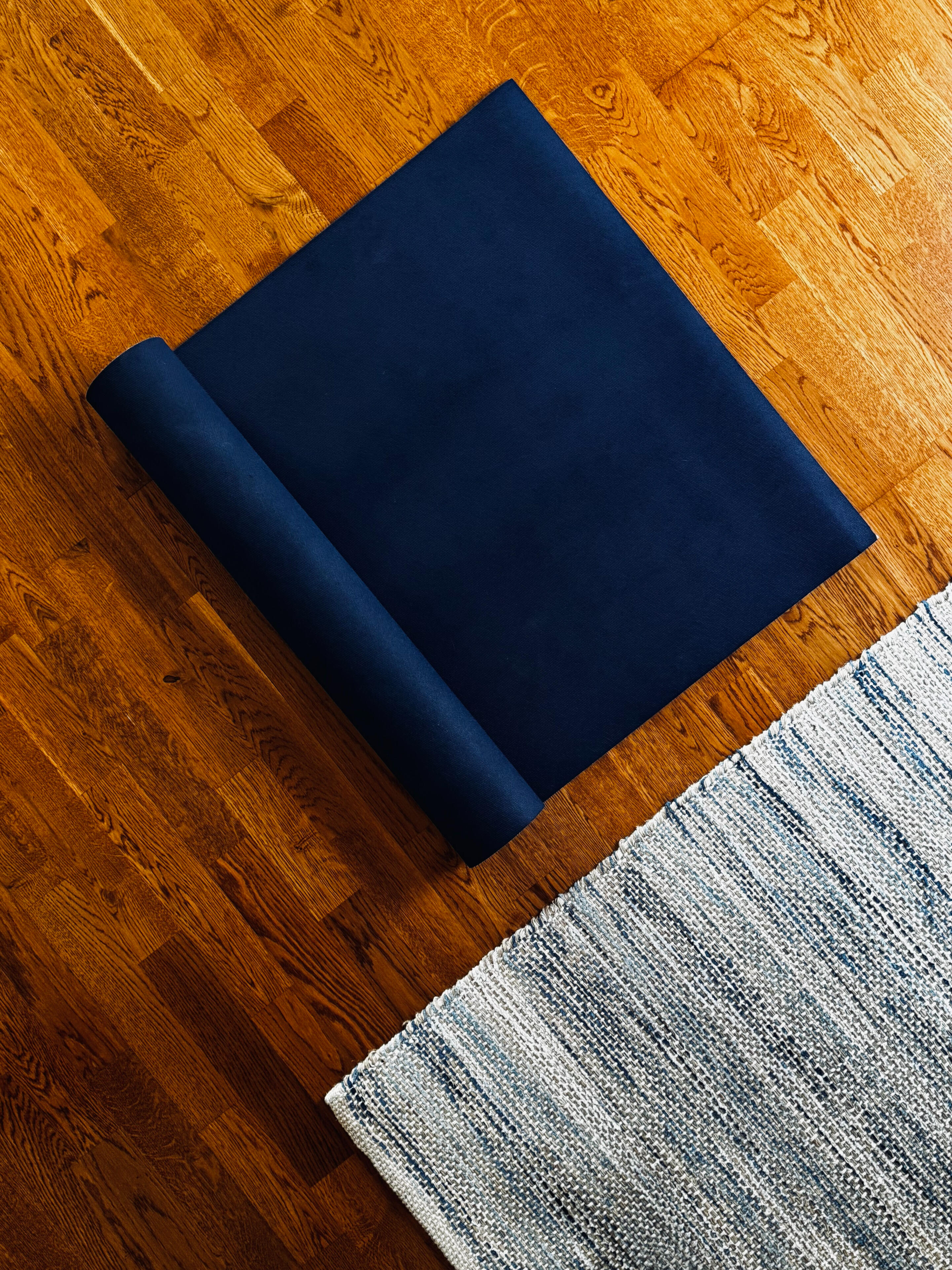 A blue yoga mat beside a blue-and-white striped rug on a hardwood floor